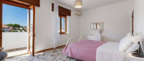 A bedroom with a bed, a dresser, a mirror, and a window with a view of buildings.