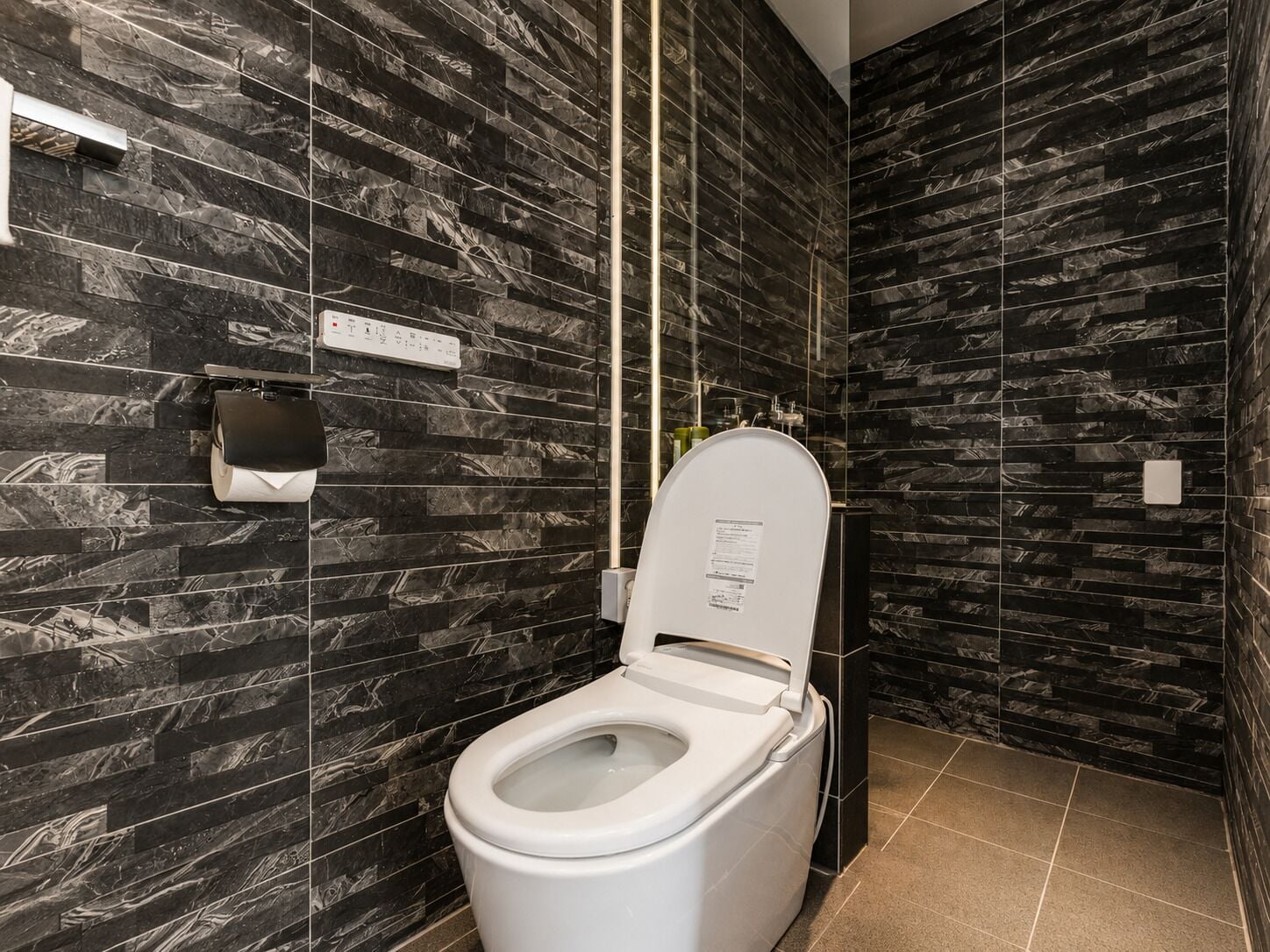 A modern bathroom with a toilet, dark marble walls, and a control panel.