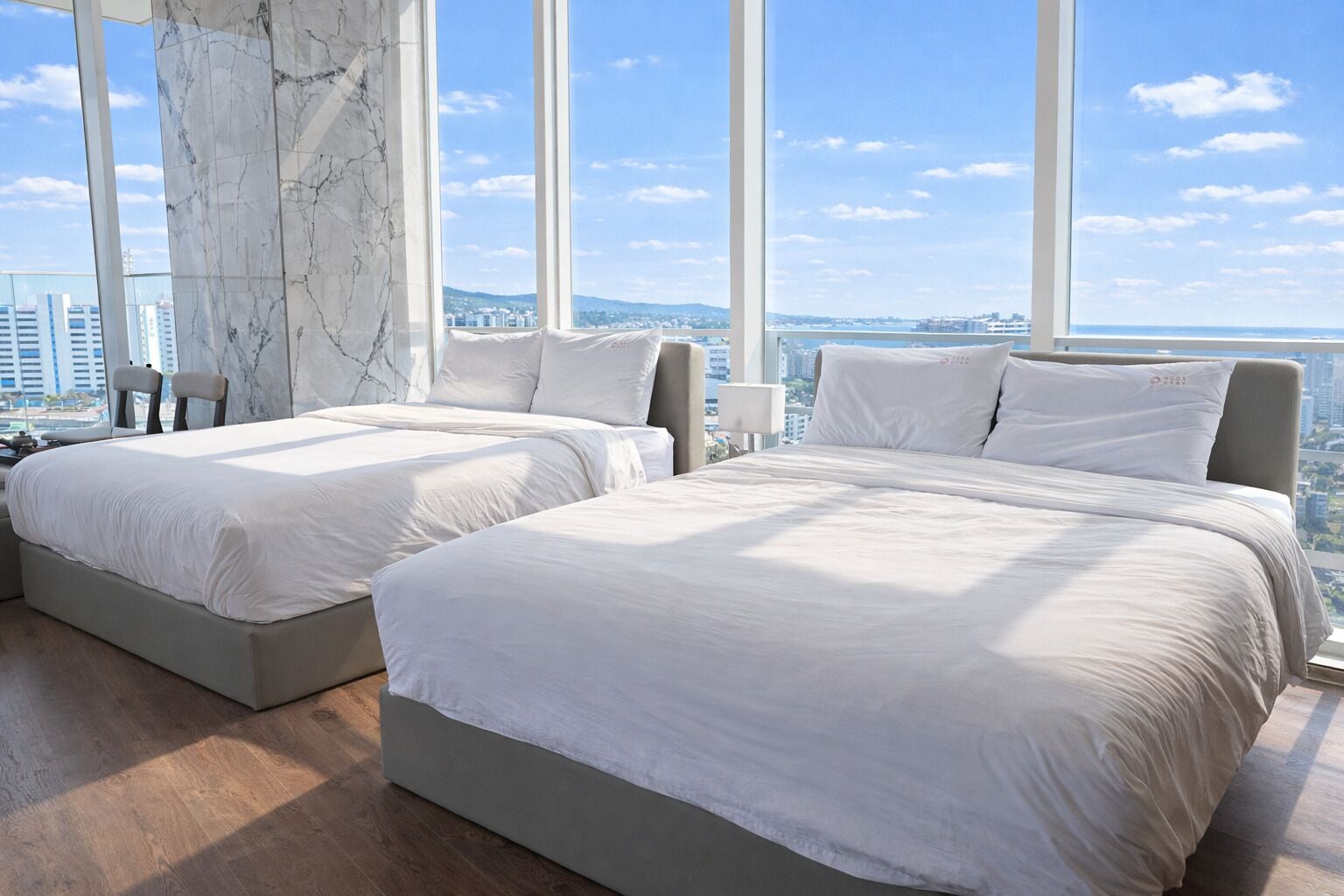 A hotel room with two beds, a marble wall, and a city view.