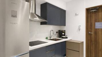 Cocina moderna con refrigerador de acero inoxidable, estufa integrada, cafetera y muebles de cocina oscuros.
