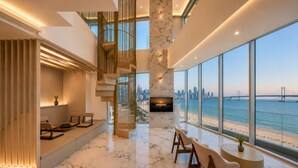 A modern living room with a large TV, a staircase, and a view of the sea.
