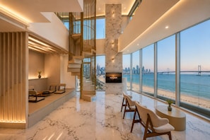 A modern living room with a large TV, a staircase, and a view of the sea.