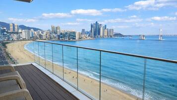 Balcón con baranda de cristal con vistas a una playa y el horizonte de la ciudad.