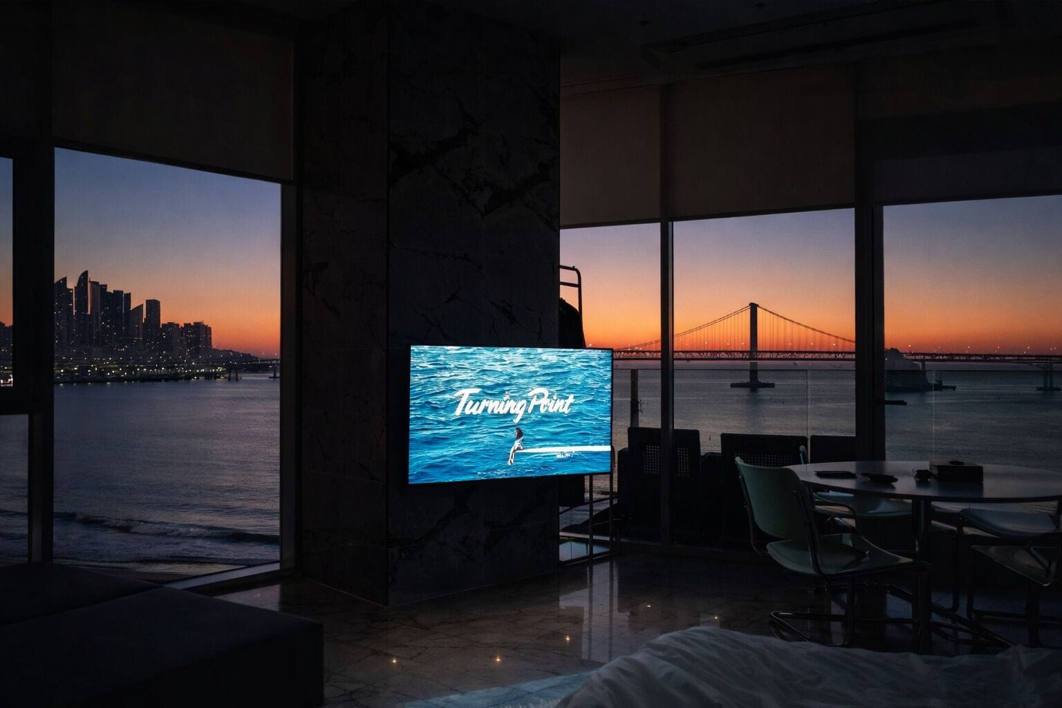Habitación moderna con una gran pantalla de televisión mostrando 'Turning Point', vistas de un horizonte urbano y un puente sobre el agua.