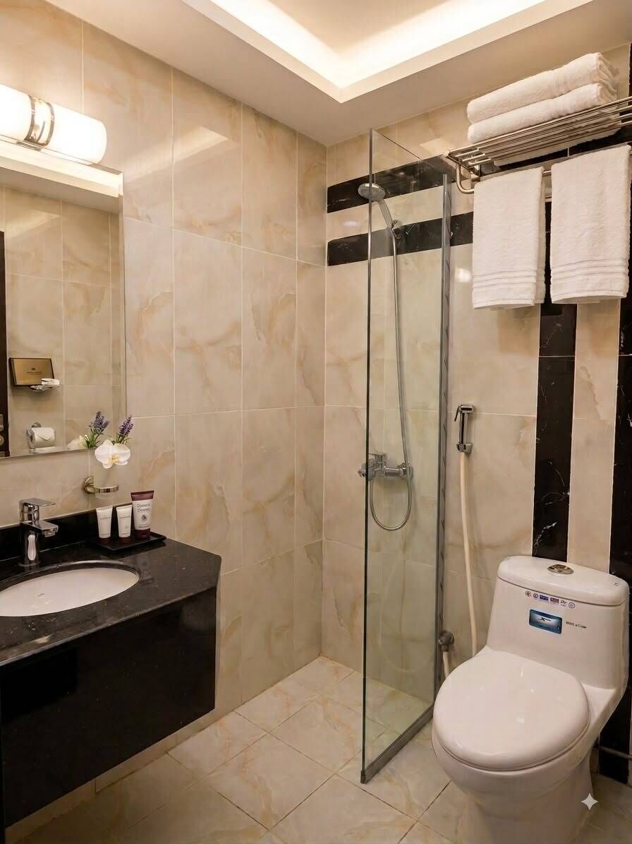 Un baño moderno con ducha envuelta en vidrio, inodoro blanco y lavamanos negro.