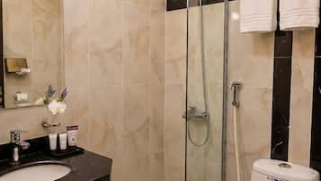Un baño moderno con ducha envuelta en vidrio, inodoro blanco y lavamanos negro.