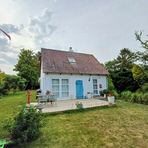 Een wit huis met een blauwe deur, een kleine tuin en een houten terras.