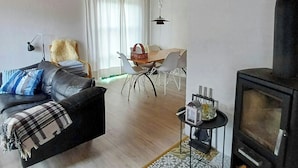 Ett vardagsrum med en soffa, ett matbord med stolar, en öppen spis och en mönstrad matta.