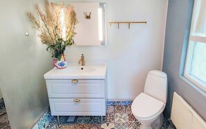 Een badkamer met een wit wastafelmeubel, toilet, spiegel en een decoratieve vaas met gedroogde planten.
