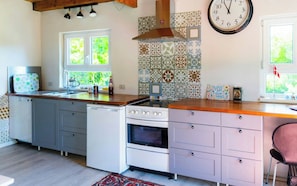 A kitchen with a stove, oven, sink, and a clock on the wall. - Cottage in the garden of Fejø Organic Food Forest (Fejø)