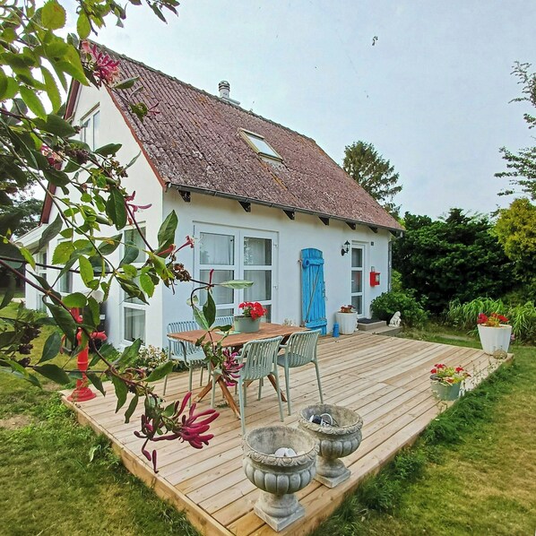 Een huis met een houten terras, een eettafel met stoelen en een blauwe deur.