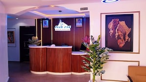 A hotel reception area with a reception desk, a reception sign, a framed artwork, and a potted plant. - Plus 234 Hotels and Suites (Ibadan)