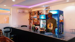 A bar area with a counter, shelves stocked with beverages, and a refrigerator. - Plus 234 Hotels and Suites (Ibadan)