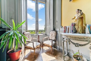 Ein Zimmer mit einem großen Fenster, einer Statue, zwei Stühlen, einem Tisch und einer Topfpflanze.