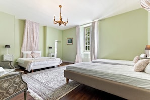 Ein Schlafzimmer mit zwei Betten, einer Deckenleuchte, einem Fenster mit Vorhängen, einem Nachttisch und einem Sessel.