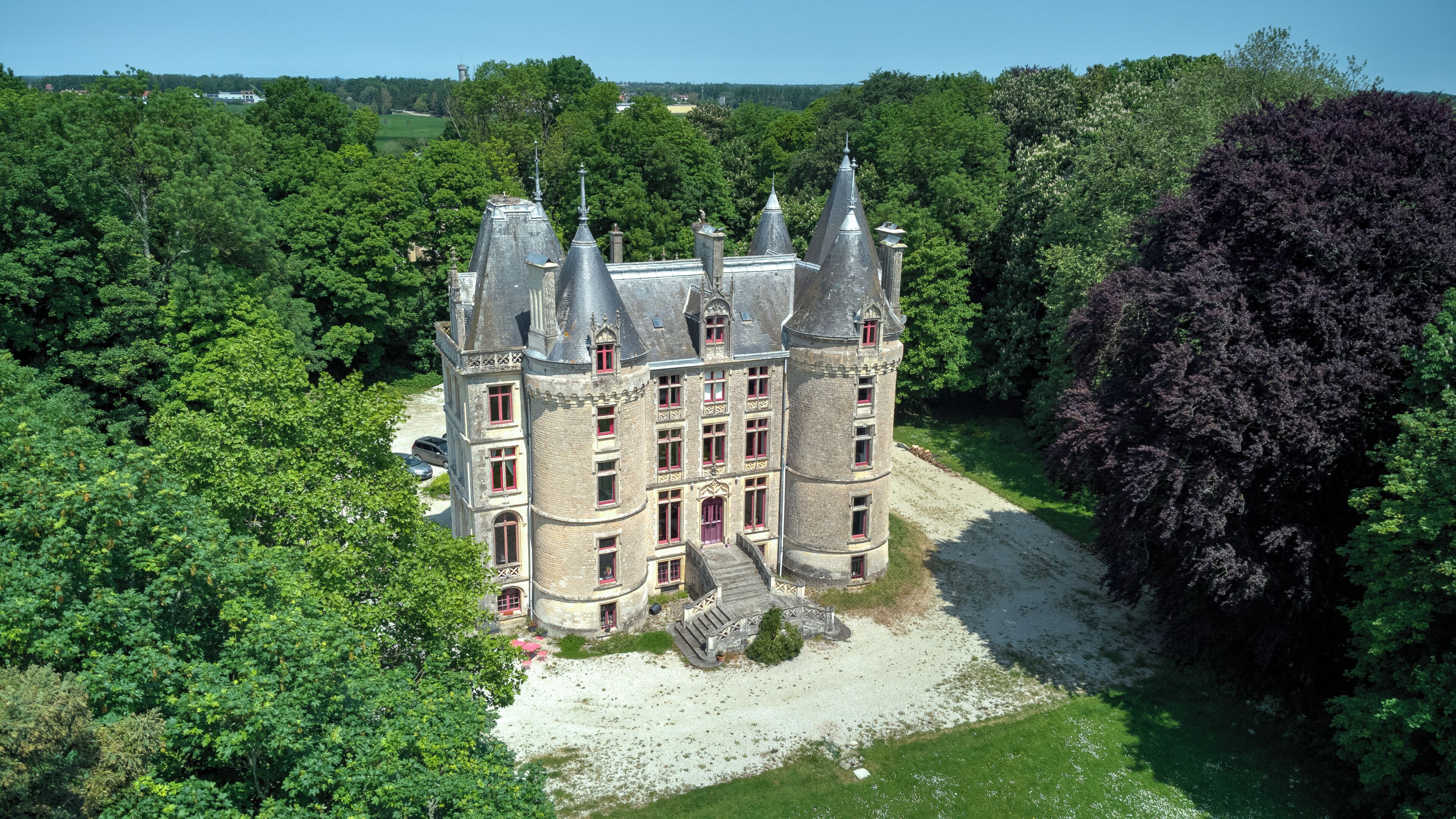 Un grand bâtiment historique doté de nombreuses tours et d’une cour centrale entourée d’une végétation luxuriante.