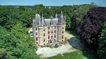 Un grand bâtiment historique doté de nombreuses tours et d’une cour centrale entourée d’une végétation luxuriante.