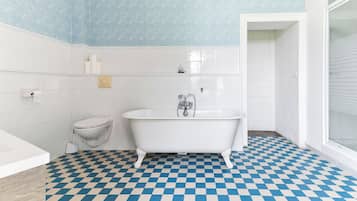 Een badkamer met een zwart-wit betegelde vloer, een witte badkuip, een toilet en een blauwe wand met patroon.