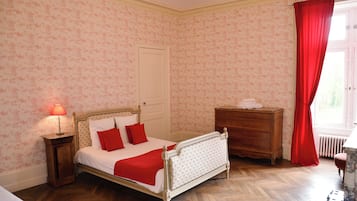 Een slaapkamer met een bed, een dressoir, een nachtkastje en een raam met rode gordijnen.