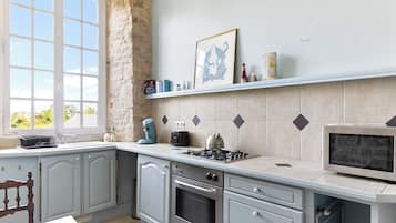 A kitchen with a stone wall, a window, a stove, and a microwave.