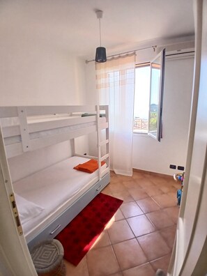 Ein Zimmer mit einem Etagenbett, einem roten Teppich, einer Deckenleuchte und einem Fenster mit Vorhängen.