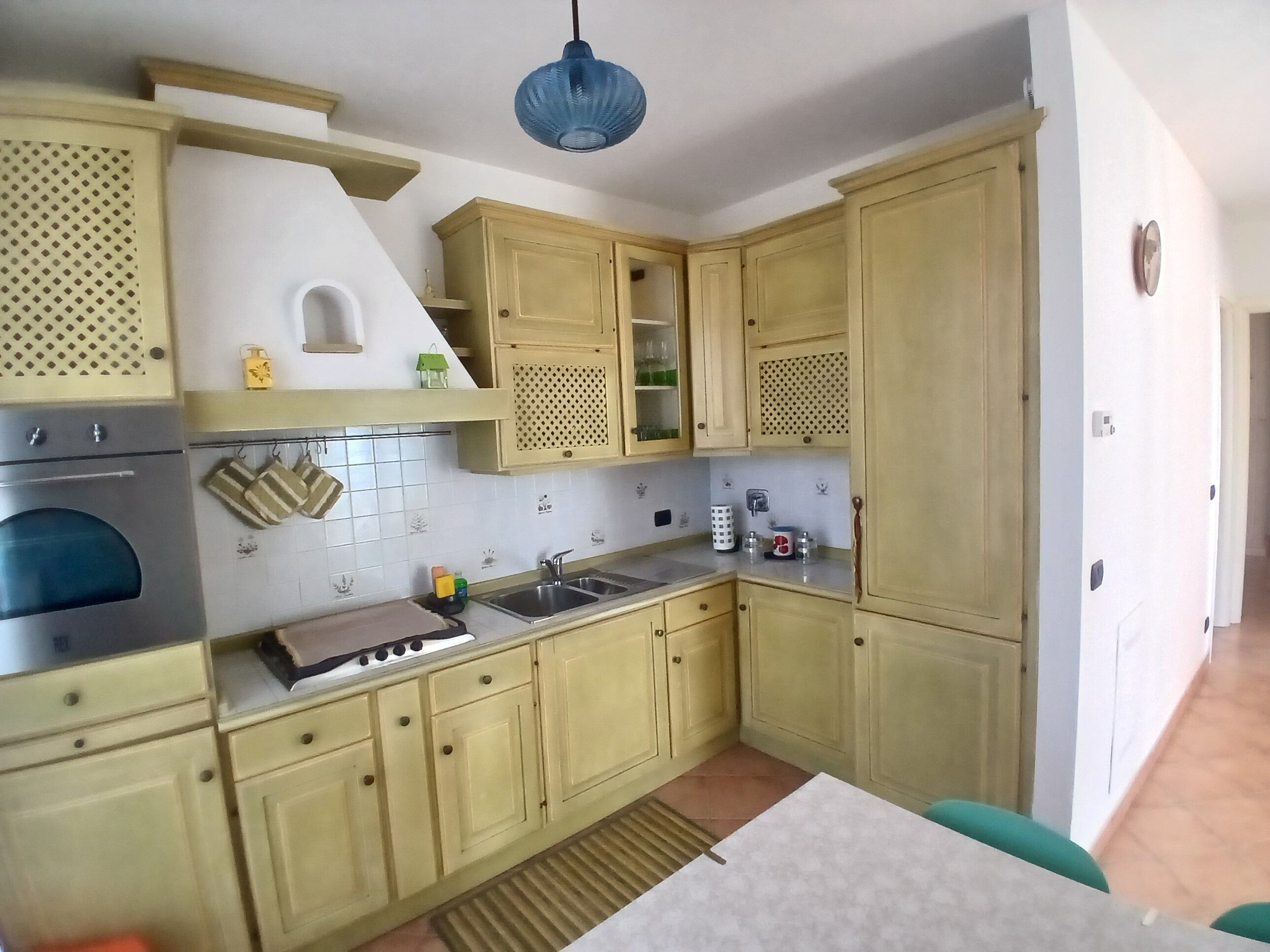 A kitchen with a stove, sink, and cabinets. There is a blue hanging light fixture above the counter.