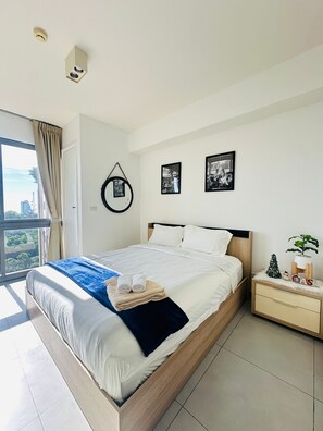 Ein modernes Schlafzimmer mit einem großen Bett, einem Nachttisch, einer kleinen Pflanze und Blick auf die Stadt.