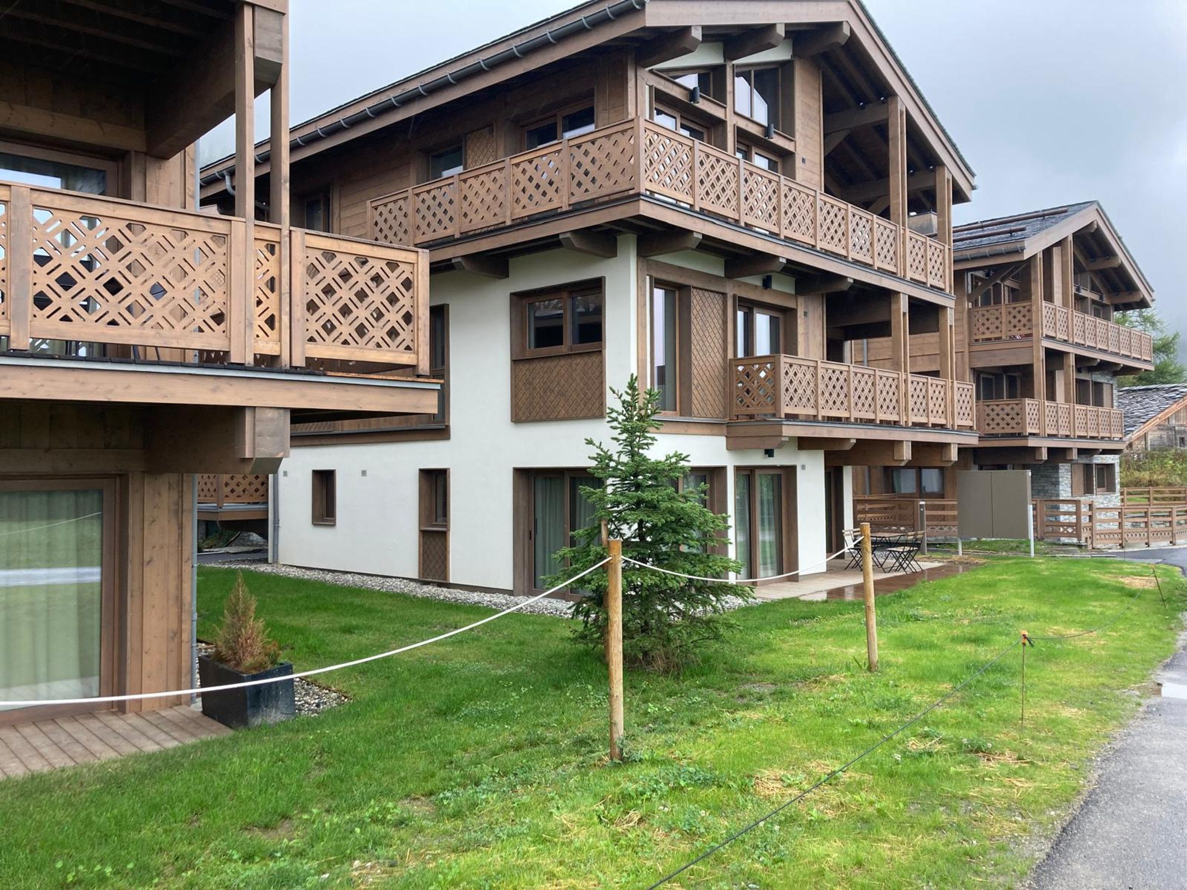 A multi-story building with balconies, wooden lattice railings, and a small tree in the foreground.