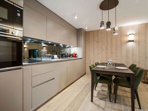 A modern kitchen with built-in appliances, a dining area with a wooden table and chairs, and a wooden wall paneling. - Ideal apartment, near slopes - 2 guests (La Tania)