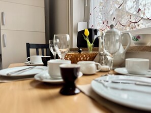 A neatly set dining table with white plates, cups, and cutlery, a vase with a yellow flower, and a decorative bowl. - Vrbo Property (Weikersheim)
