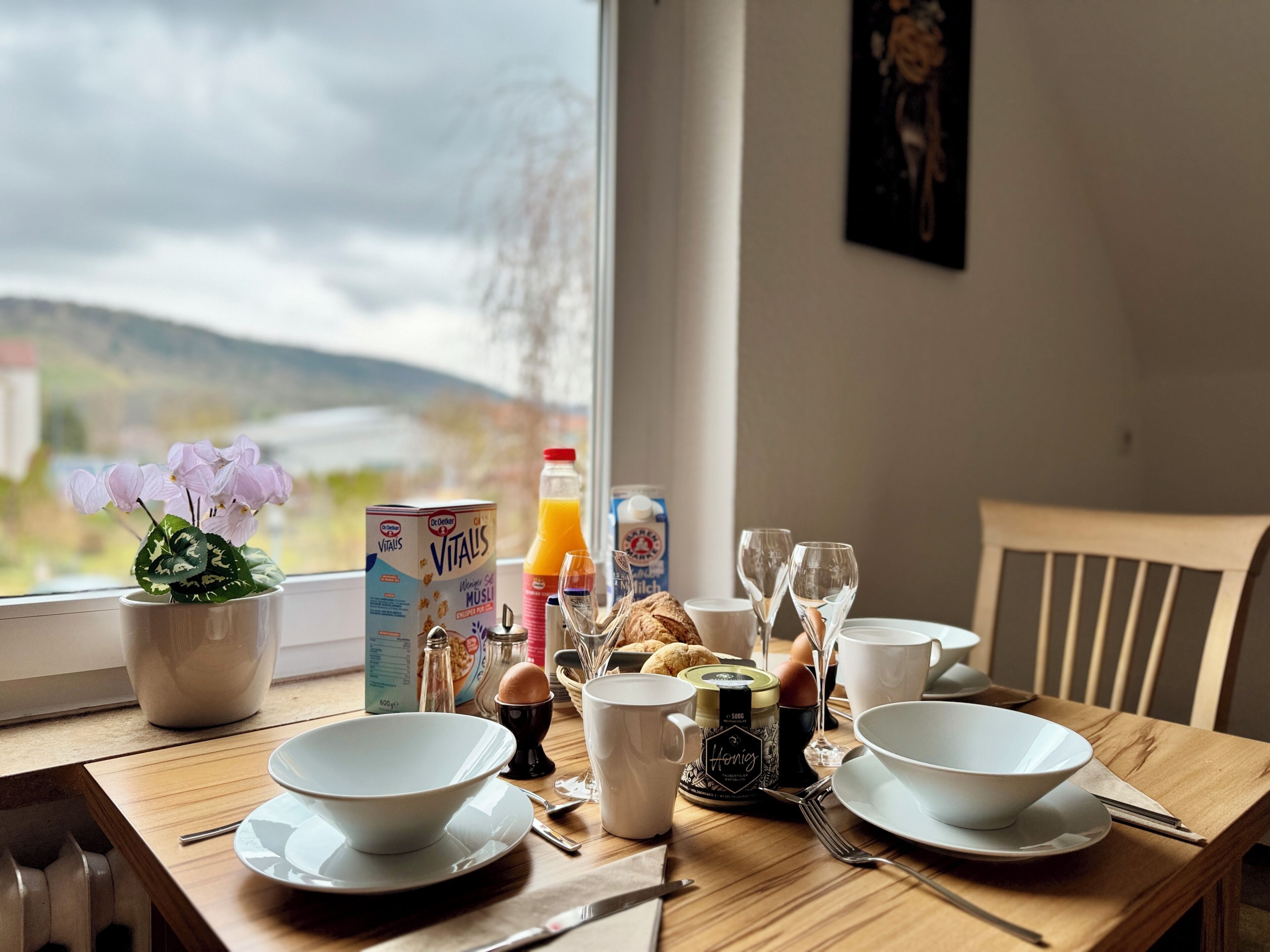 A breakfast table with bowls, a bottle of orange juice, a carton of milk, and a potted plant.
