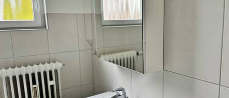 Een badkamer met een witte wastafel, een spiegel en een radiator.
