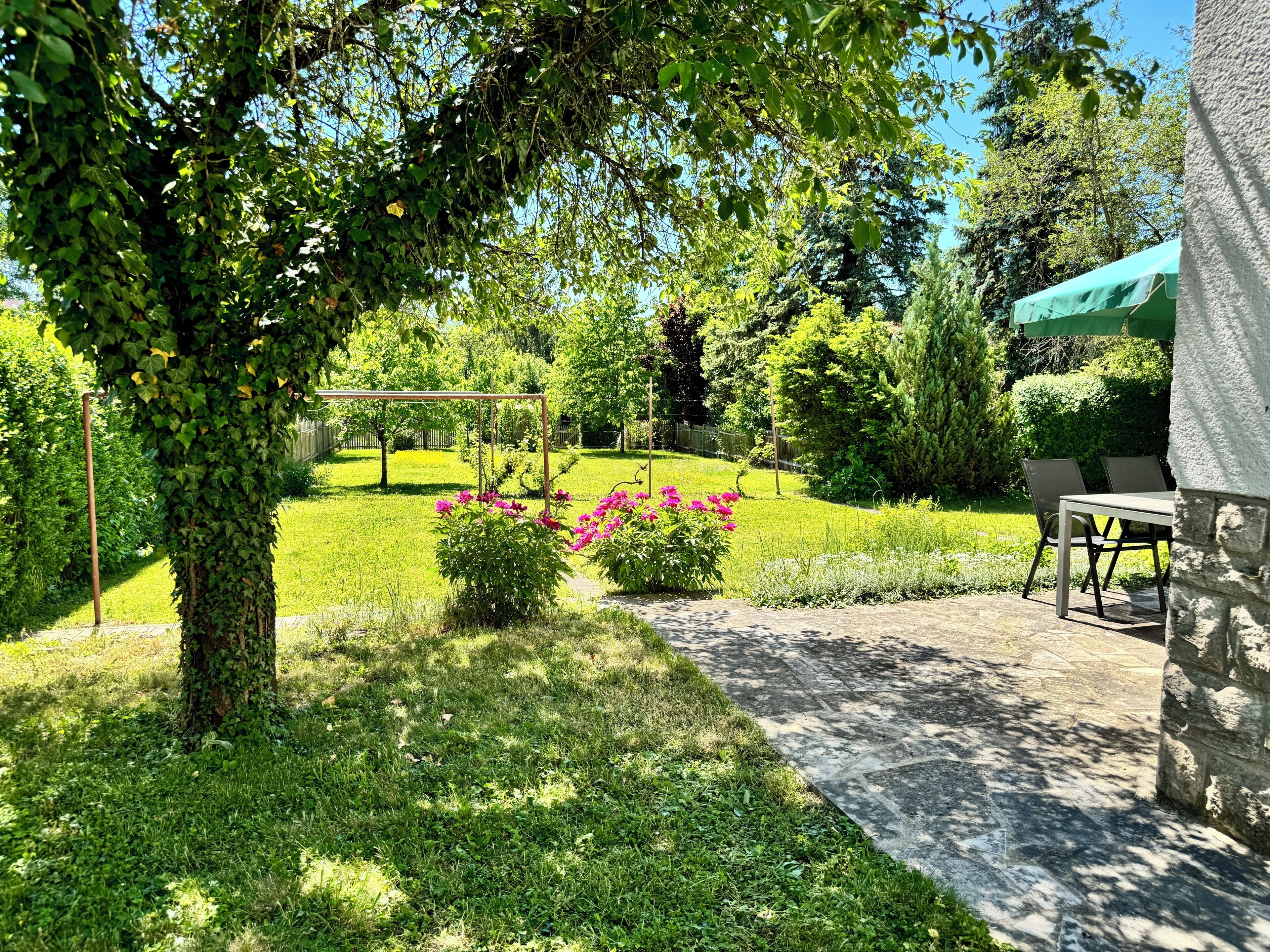 A garden with a pergola, a stone wall, and a table with chairs.