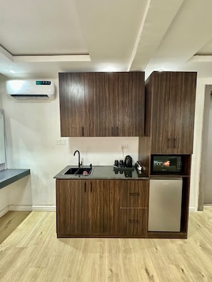 A compact kitchen with wooden cabinets, a built-in microwave, and a small refrigerator. - Timeoak signature Hotel (Abuja)