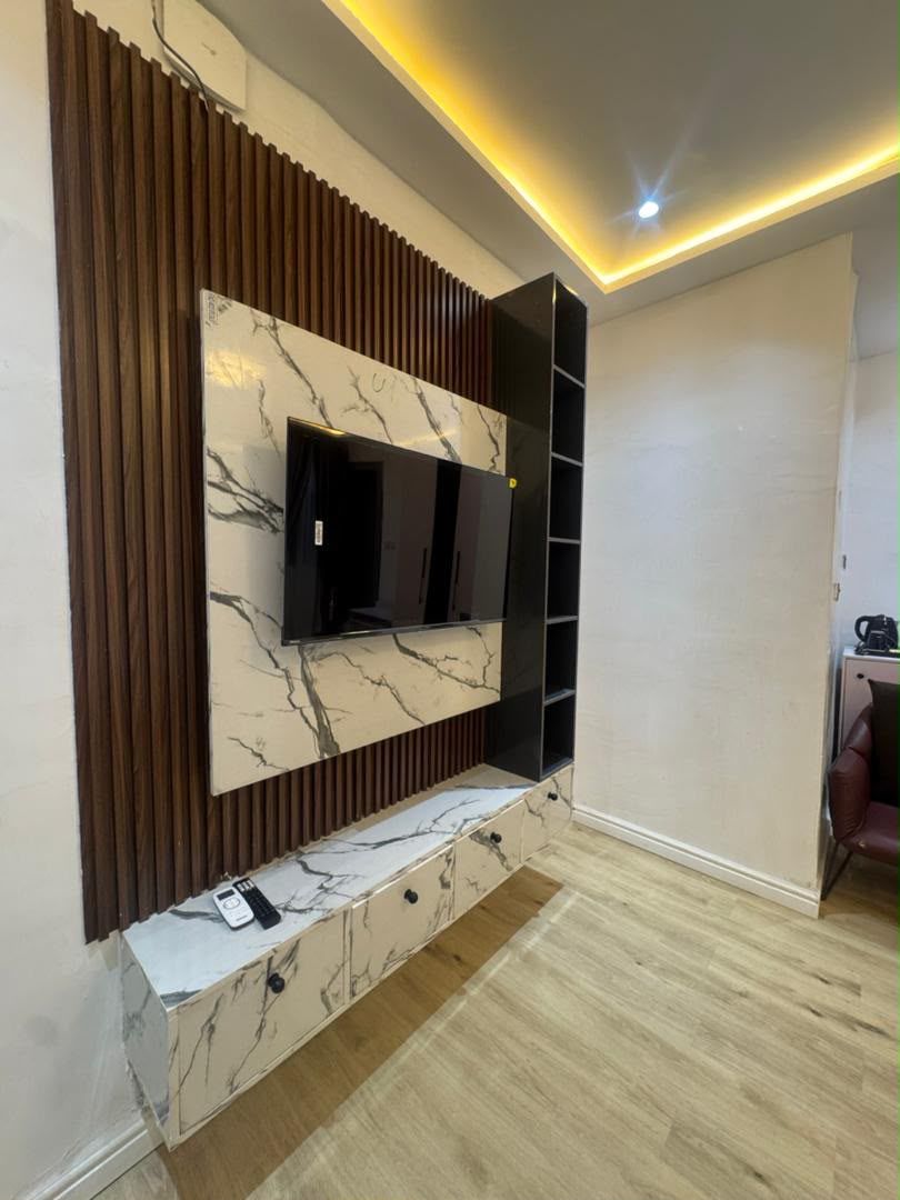 Un salon moderne avec un mur d’accent en marbre, des étagères intégrées et un téléviseur à écran plat.