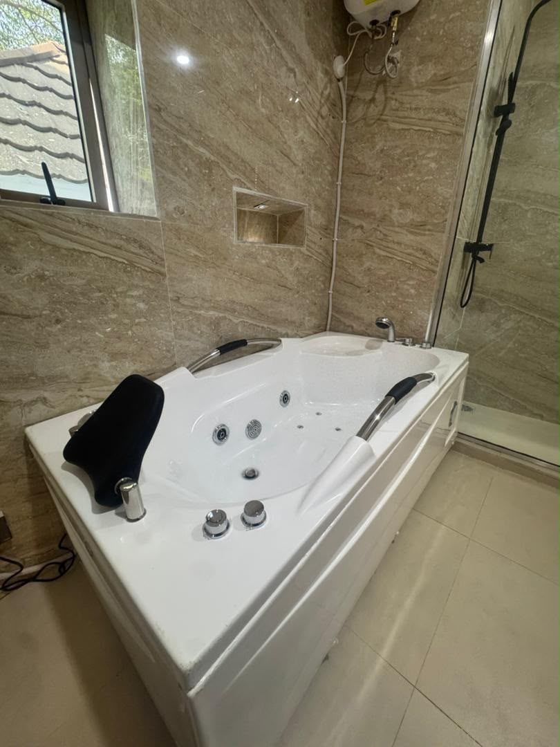 A bathroom with a large white bathtub, a shower area, and a window.
