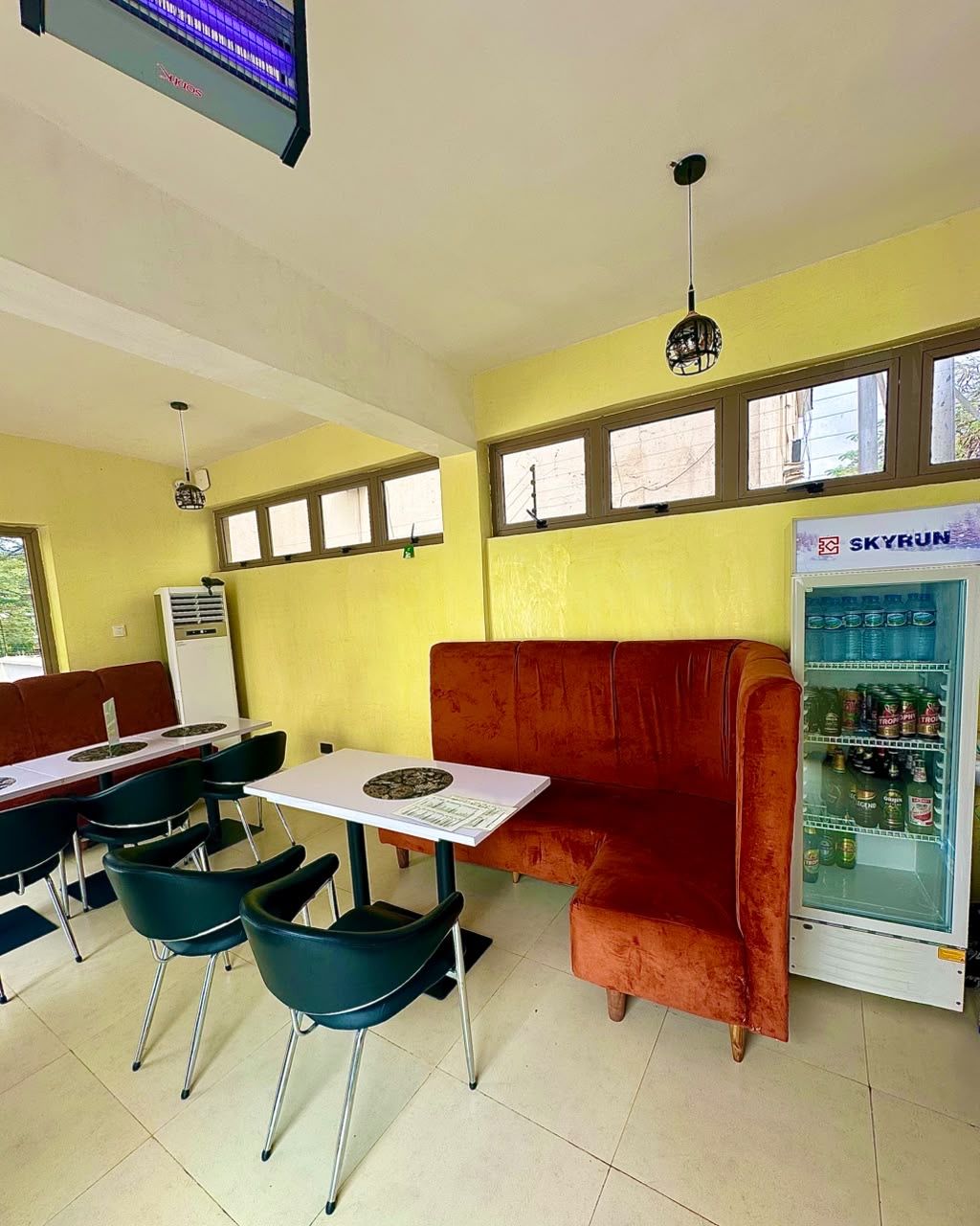 A restaurant interior with booths, tables, chairs, a ceiling fan, a TV screen, and a refrigerator.