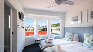 Camera d'albergo con un letto, due sedie, una scrivania, una TV e ampie finestre con vista sull'esterno.