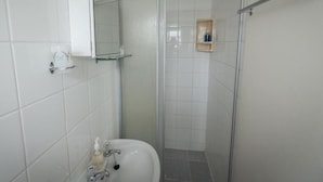 Un bagno con un lavandino bianco, uno specchio e un box doccia.