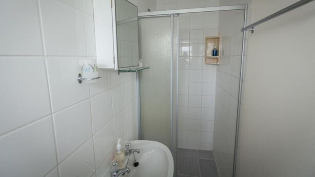 A bathroom with a white sink, a mirror, and a shower enclosure. - Cape Agulhas Guesthouse (L'Agulhas)