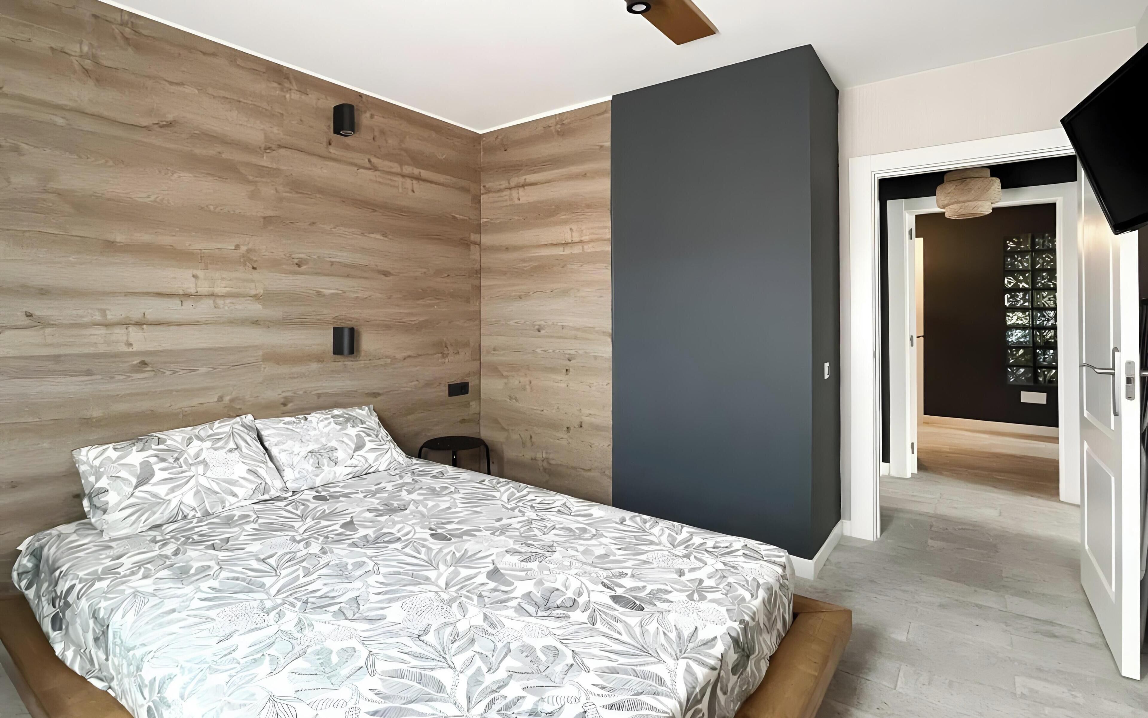Un dormitorio con cama, paneles de madera en la pared, una pared de acento gris y una puerta que da a otra habitación.