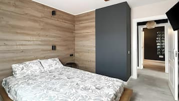 Un dormitorio con cama, paneles de madera en la pared, una pared de acento gris y una puerta que da a otra habitación.