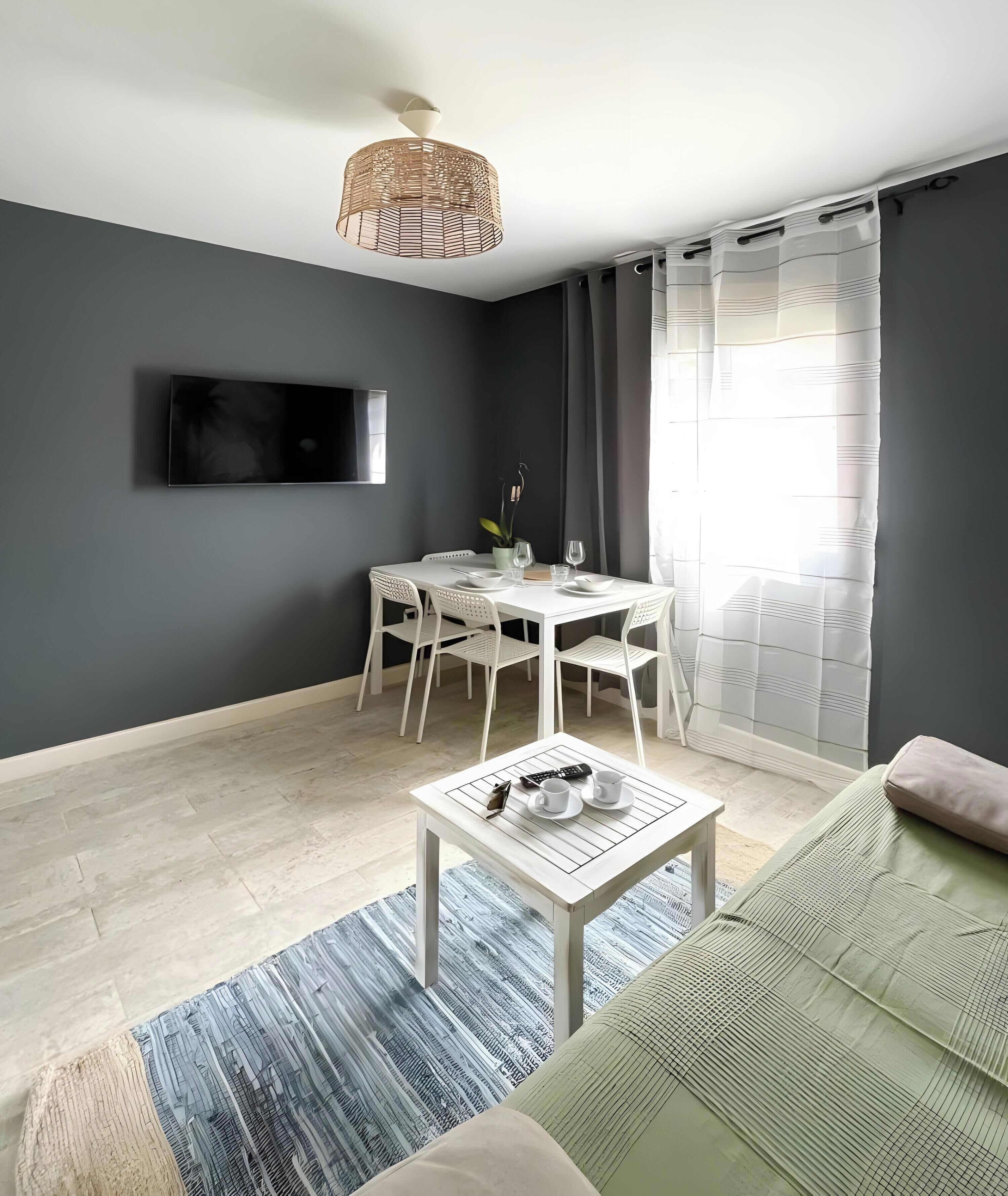 Uma sala de estar moderna com televisão de tela plana, uma mesa de jantar com cadeiras, uma mesa de centro e um sofá.
