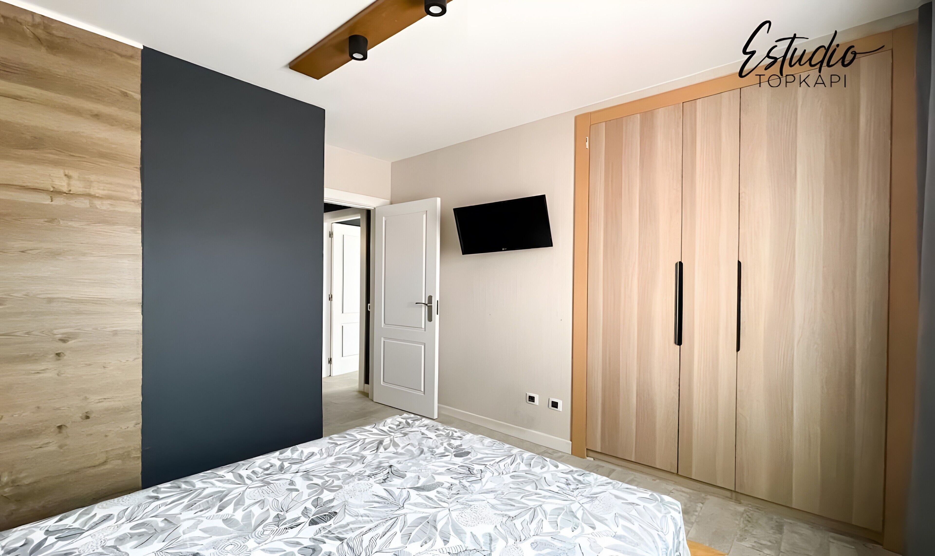 Ein Schlafzimmer mit Bett, Kleiderschrank, Fernseher und einer Tür zu einem weiteren Raum.
