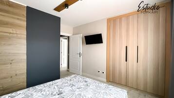 Ein Schlafzimmer mit Bett, Kleiderschrank, Fernseher und einer Tür zu einem weiteren Raum.