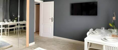 Une chambre moderne dotée d’un coin repas, d’un téléviseur fixé au mur et d’un grand miroir qui agrandit visuellement l’espace.