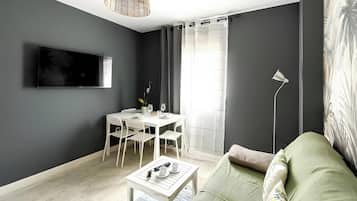 Una sala moderna con comedor, un televisor de pantalla plana montado en la pared, una lámpara de pie y un sofá con un cojín estampado.