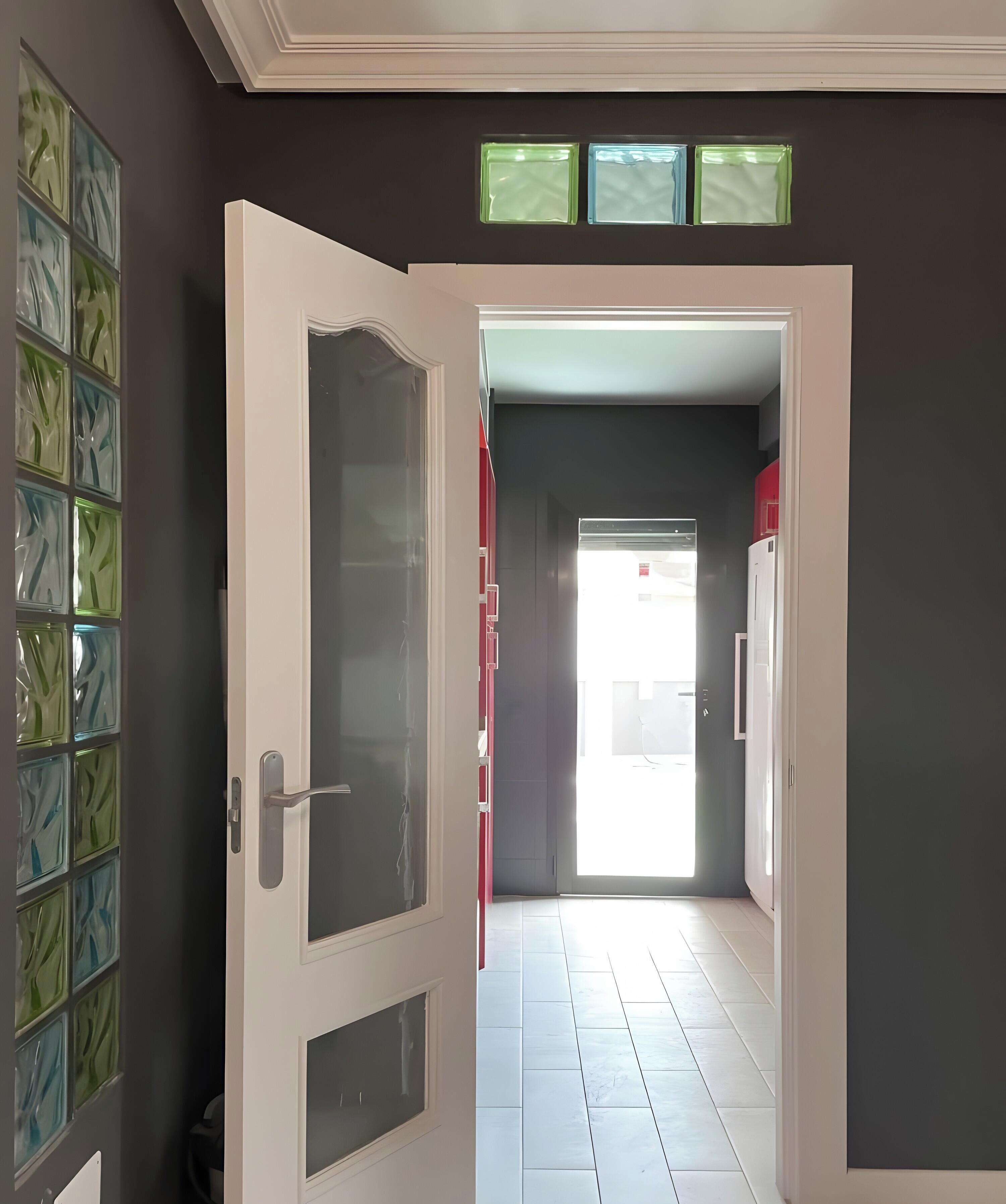 Un pasillo interior con una puerta que da a una habitación luminosa.