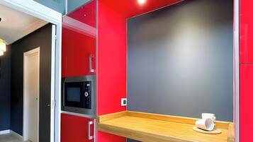 Een moderne keuken met rode kastjes, een magnetron en een houten plankje met een beker.
