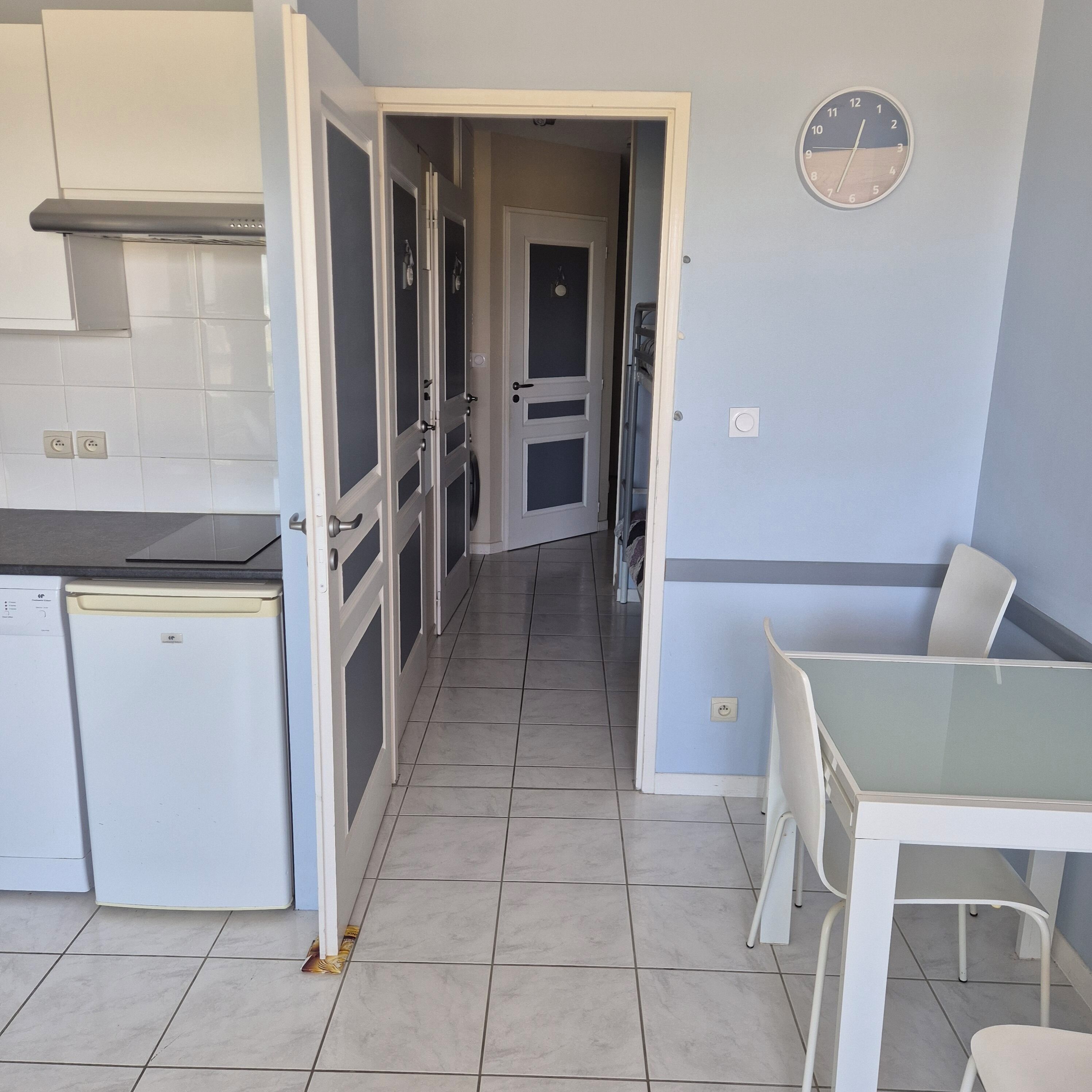 Una cocina con comedor, un reloj en la pared y una puerta que da a otra habitación.
